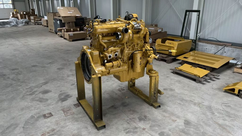 Gold-colored engine block on a trolley mount standing on the concrete floor of a hall. Cardboard boxes can be seen in the background