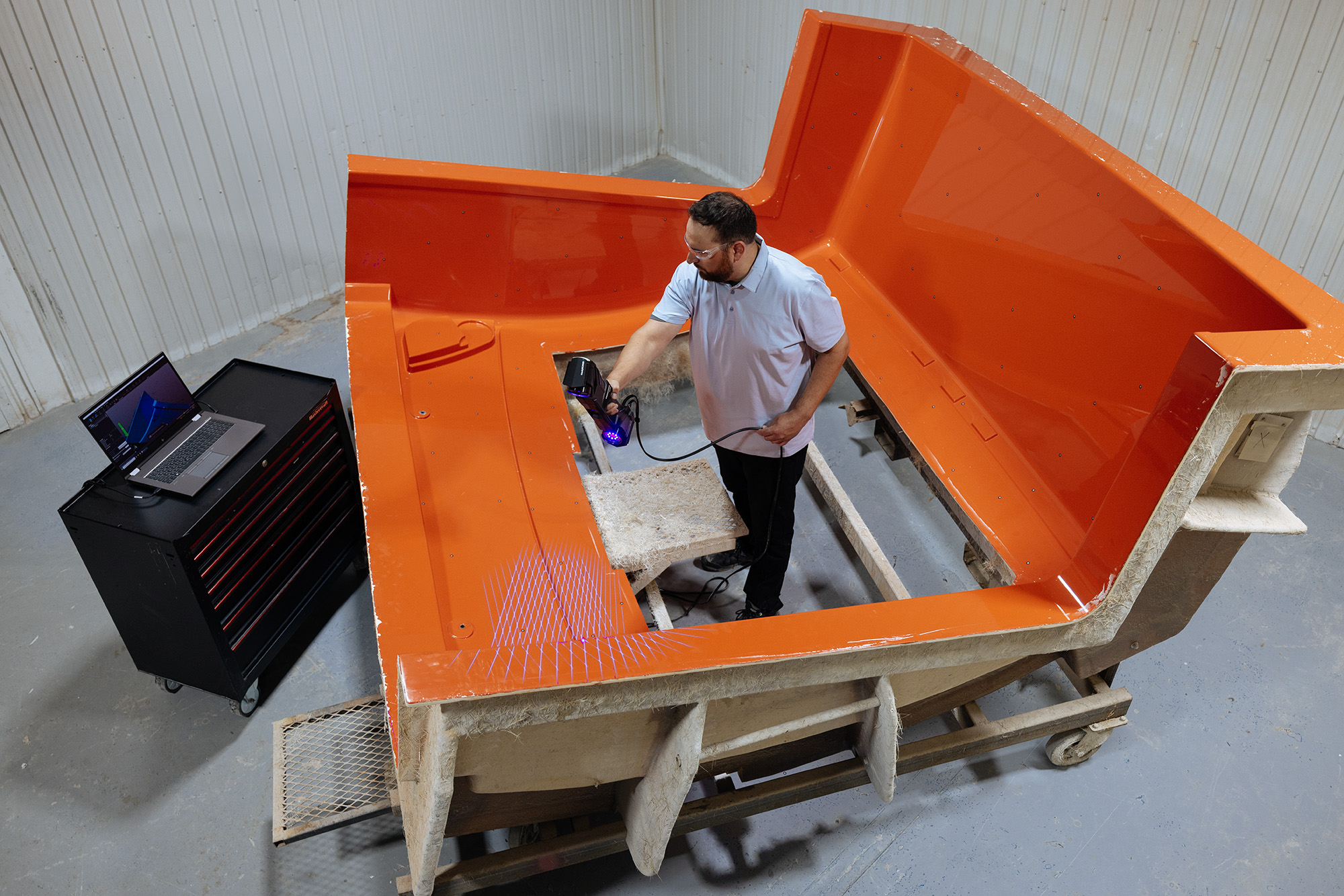 Engineer in the middle of a gigantic part making twice his size, using the Creaform HandySCAN 3D|MAX Series to scan the part while looking at the 3D model on a laptop screen.