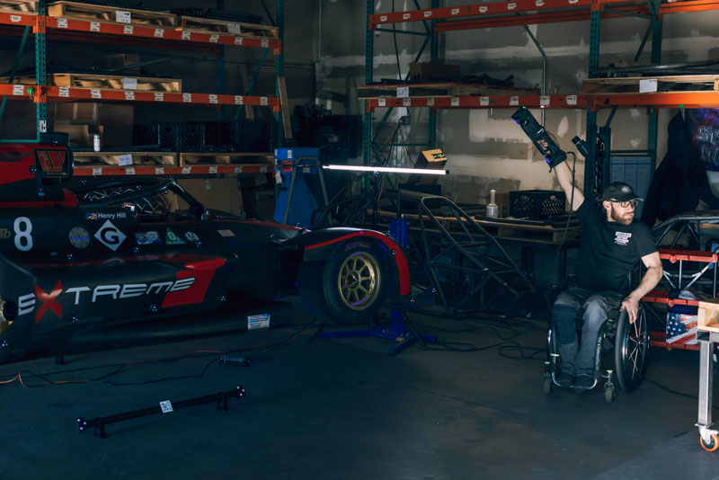 Man in a wheelchair using the Go!SCAN 3D scanner to measure a race car inside a garage