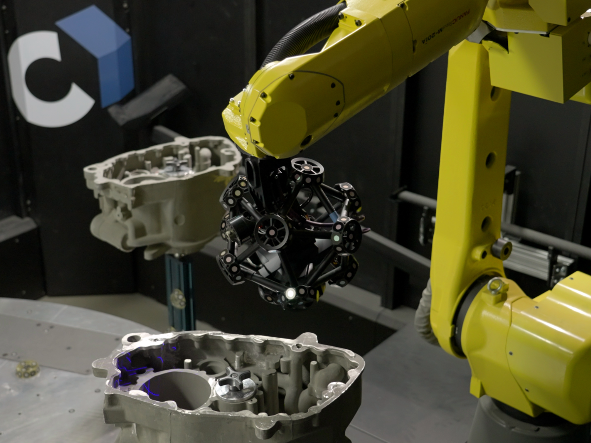 El escáner MetraSCAN 3D-R montado en un robot Fanuc en una celda Cube-R midiendo una serie de cajas de engranajes