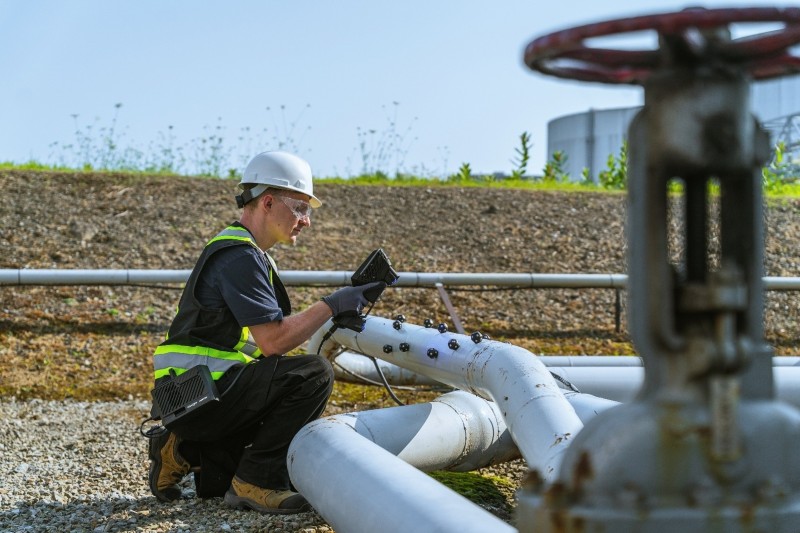Inspección de tuberías industriales al aire libre con un trabajador utilizando el HandySCAN EVO|Elite en tuberías blancas marcadas con objetivos de referencia.