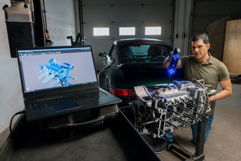 Ingenieur scannt mit der HandySCAN 3D|PRO-Serie einen Motorblock. Das 3D-Mesh wird auf dem Computerbildschirm angezeigt.