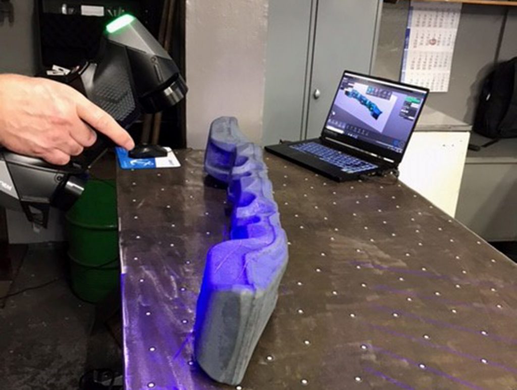 HandySCAN 3D BLACK utilizado para escanear componentes forjados en una mesa con una computadora portátil en el fondo que muestra VXelements