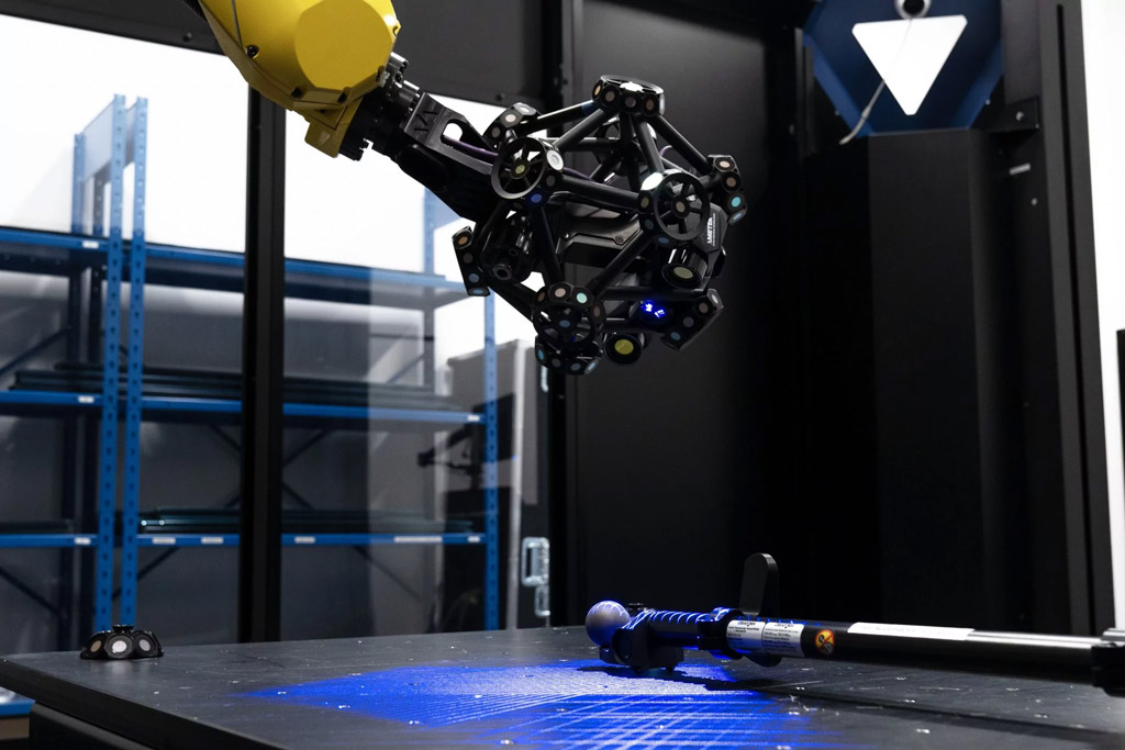 Un MetraSCAN 3D-R escáner óptico CMM, montado en robot que mide una herramienta de calibración en una celda de metrología