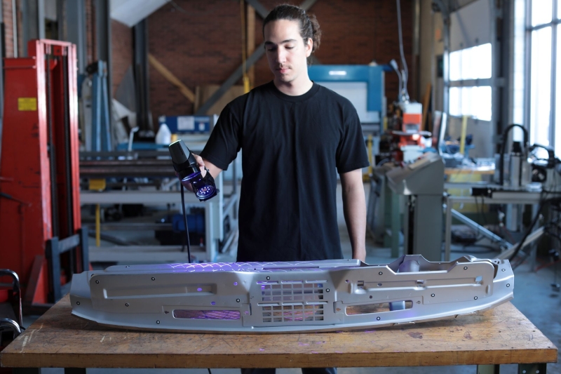 操作人员在工业车间内使用手持式 3D 扫描仪扫描大型金属物体