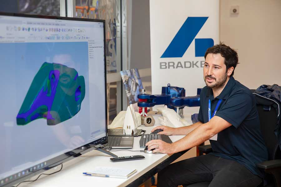 Un dipendente Bradken seduto a un tavolo davanti a un grande schermo che mostra il modello di un dente della benna di un escavatore nel software Scan-to-CAD. 