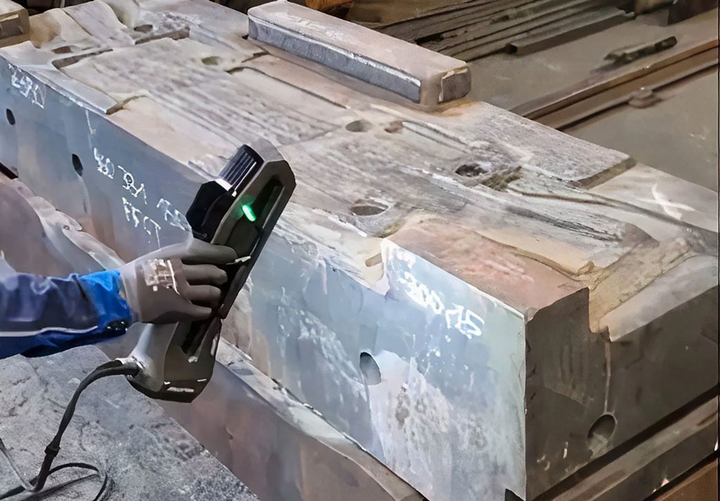 左起：一只戴着灰色手套的手里拿着一台 Go!SCAN 3D 扫描仪，用来扫描卡车车轴的锻造模。