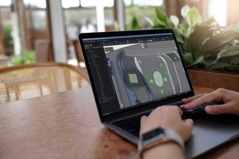Una persona sentada en una mesa utilizando un ordenador portátil visualizando una pieza en el módulo de inspección del paquete de metrología de Creaform.