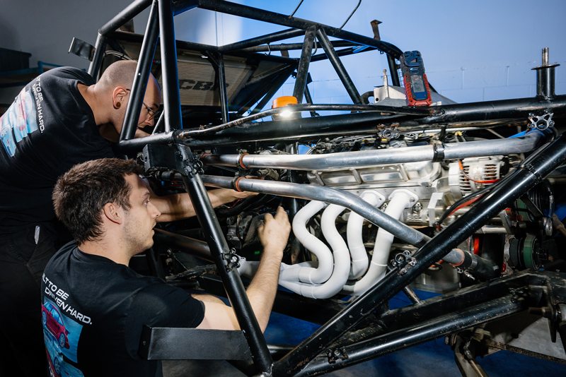 两名 EP9 Autosport 技术人员正在车辆底盘下，将新歧管安装到赛车发动机上。