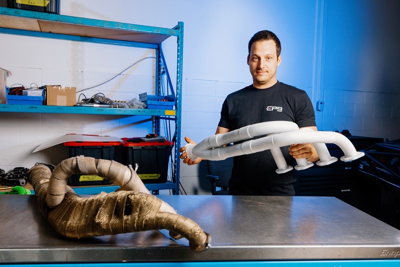 EP9 Autosport 的机械师正在车间工作台上，对比带有陶瓷隔热涂层的新歧管与传统包裹式歧管。