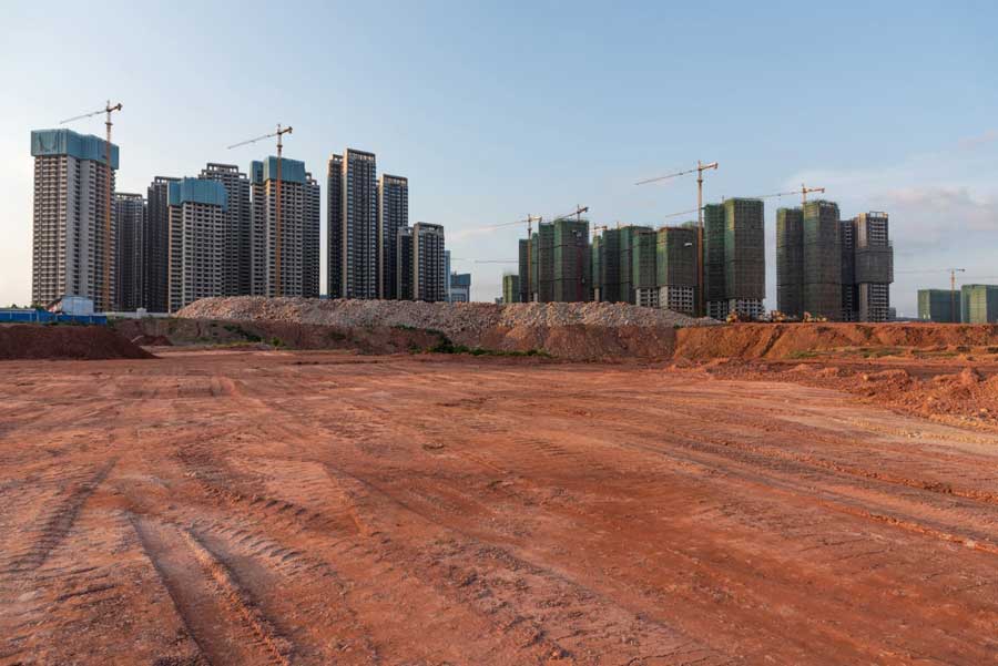 Diversi edifici di grandi dimensioni circondati da grandi gru gialle con un vasto cantiere sullo sfondo