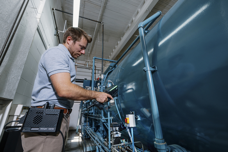 Operador inspeccionando un gran tanque industrial con el HandySCAN 3D|Serie EVO y el kit de movilidad en el área de producción, cerca de vibraciones y en espacios reducidos.