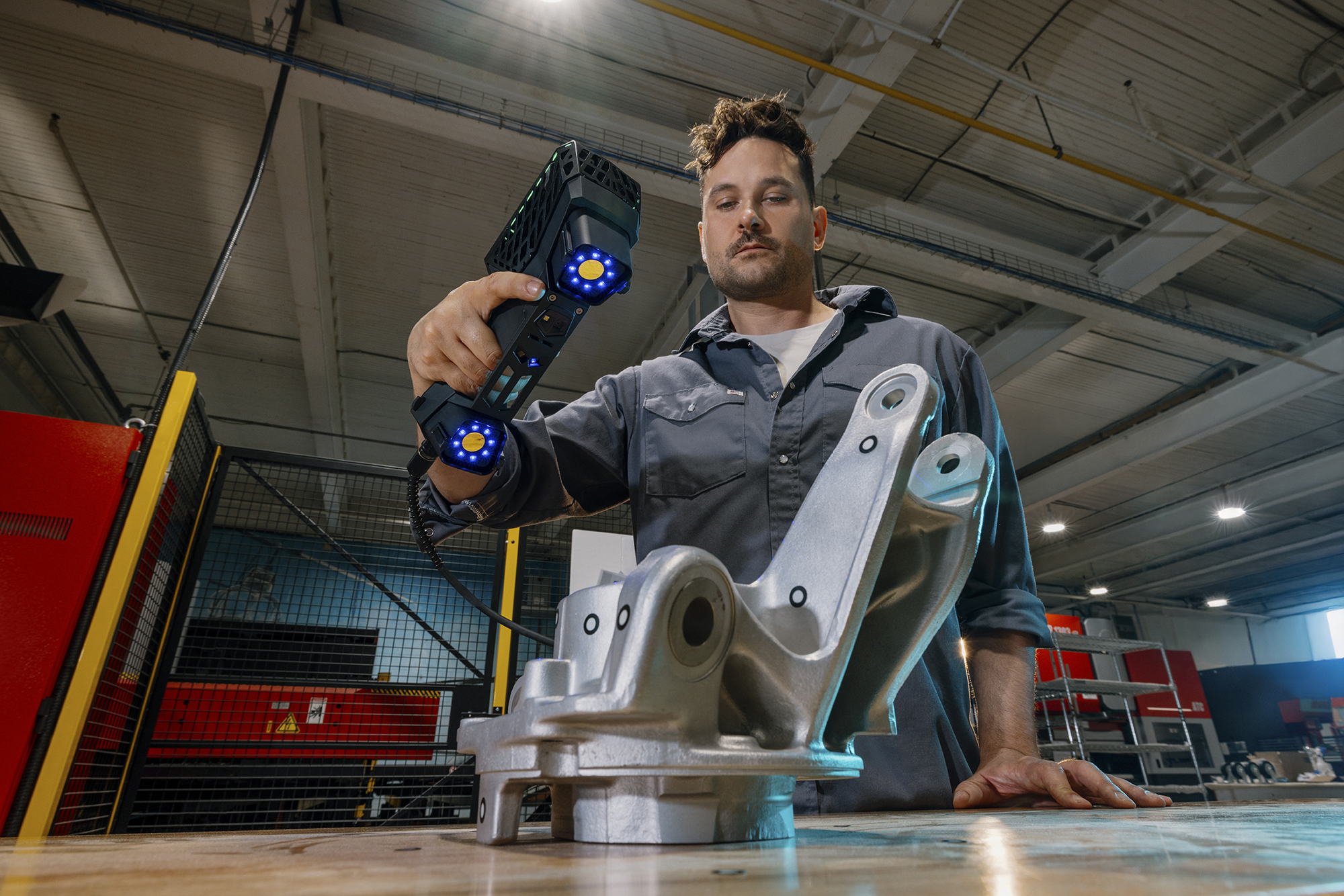 Operatore che utilizza uno HandySCAN 3D|Serie EVO con certificazione ISO per ispezionare un pezzo industriale in ambiente di produzione.