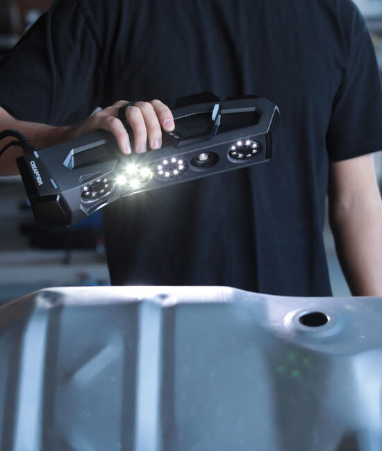 Technician using a Creaform Go!SCAN 3D scanner to capture detailed surface data of an industrial component, with bright LED lights illuminating the scanning area.