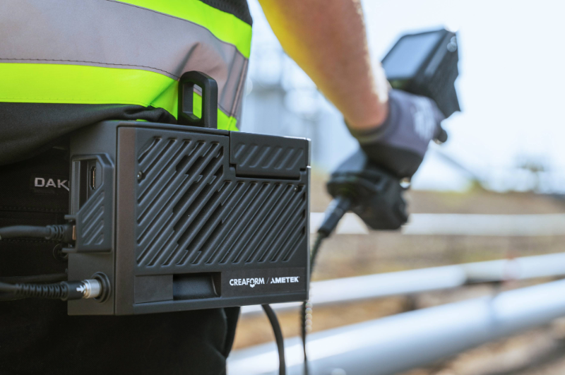 Operator wearing a high-visibility vest using a Creaform Mobility Kit connected to a handheld scanner for industrial inspection