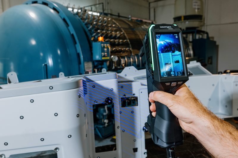 Close-up of EVO Series 3D scanner projecting blue laser lines while scanning a part with the autoclave in background