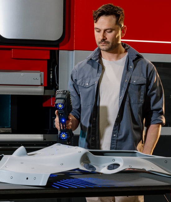 Person holding EVO Series 3D scanner near a large molding part on a workbench in an industrial setting