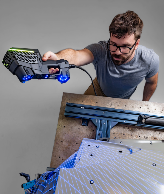 Person using EVO Series 3D scanner with blue laser pattern on a sheet metal part.