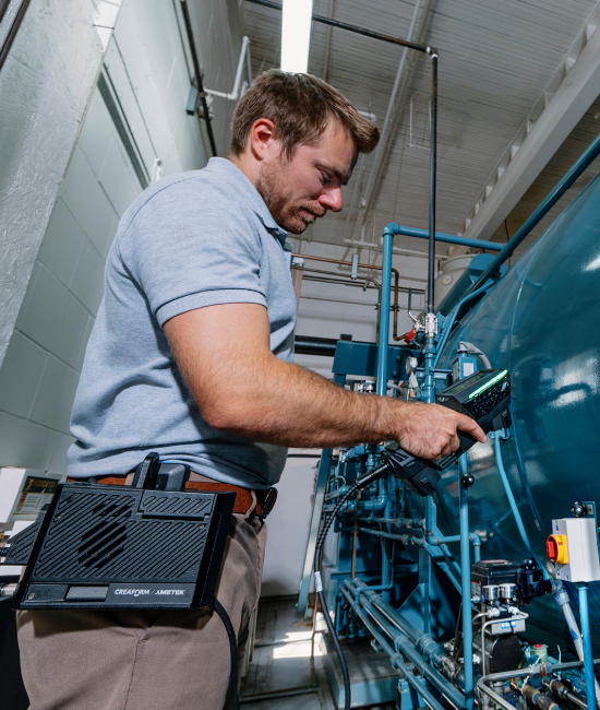 A person operating an EVO Series 3D scanner connected to the Mobility Kit, inspecting a large cylindrical industrial machine