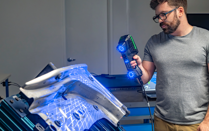 EVO Series 3D scanner emitting blue laser lines while scanning a reflective black surface in an industrial setting.