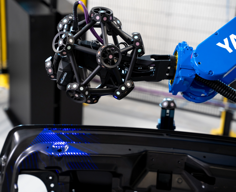 Blue Yaskawa robotic arm with MetraSCAN 3D scanner inspecting a black automotive part with blue laser lines
