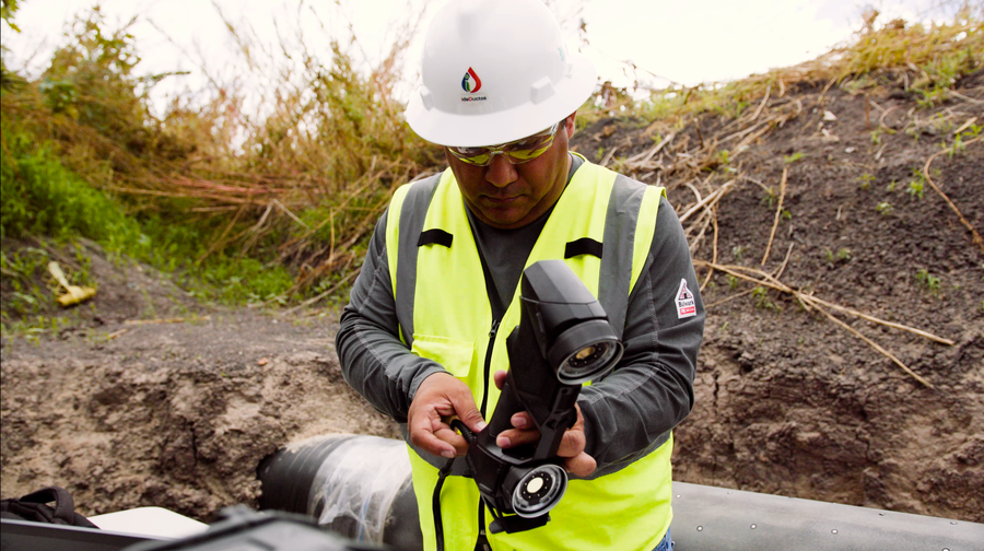 Integridad de Ductos employee in a yellow safety vest and white hard hat is connecting the HandySCAN BLACK|Elite in a ditch, next to the pipeline