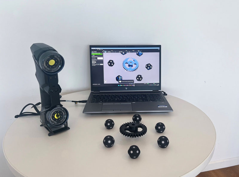 テーブル上に並ぶ、スキャンデータからCADデータにして3Dプリントされた完全な歯車と、その周囲に配置された360°ターゲット、 HandySCAN BLACK+|Elite、それとScan-to-CAD Proモジュールを表示するノートパソコン。