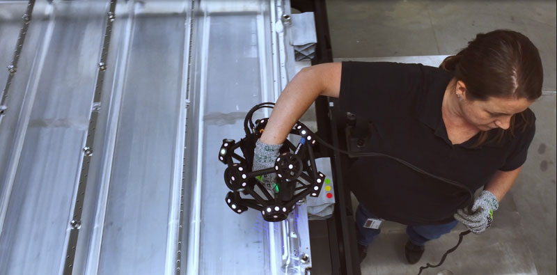 Vista desde arriba de un empleado utilizando el escáner MetraSCAN 3D para inspeccionar la bandeja de una batería de coche