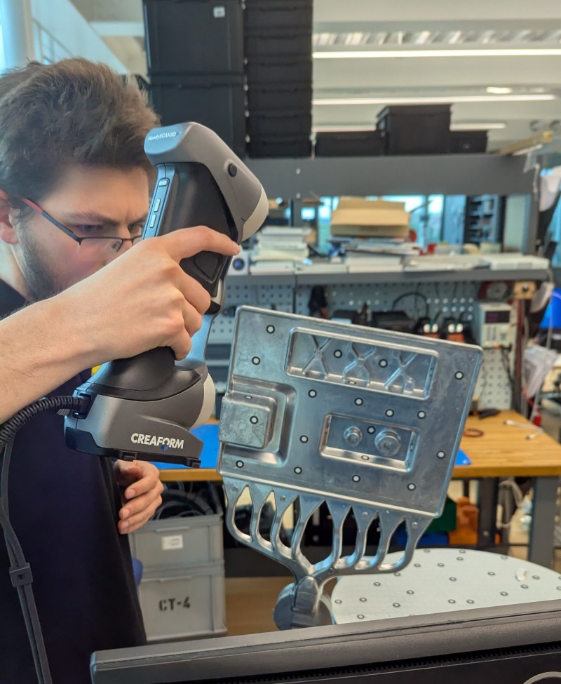 Mitarbeiter nutzt den HandySCAN 3D von FARO CREAFORM zur präzisen 3D Erfassung eines metallischen Bauteils im Werkstatt  und Prototyping Umfeld.