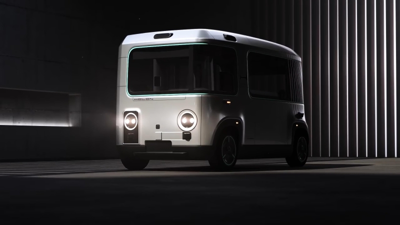 Navette urbaine électrique autonome HOLON exposée dans un cadre architectural moderne, avec des phares LED circulaires et un design minimaliste et épuré.