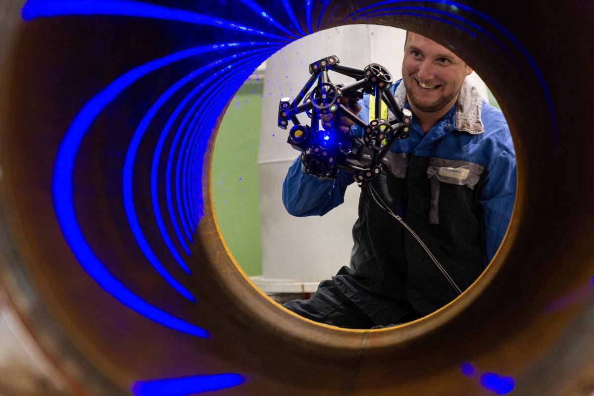 一名男子用 MetraSCAN 3D 扫描一个管道的内部。您可以看到管内的蓝色激光线。